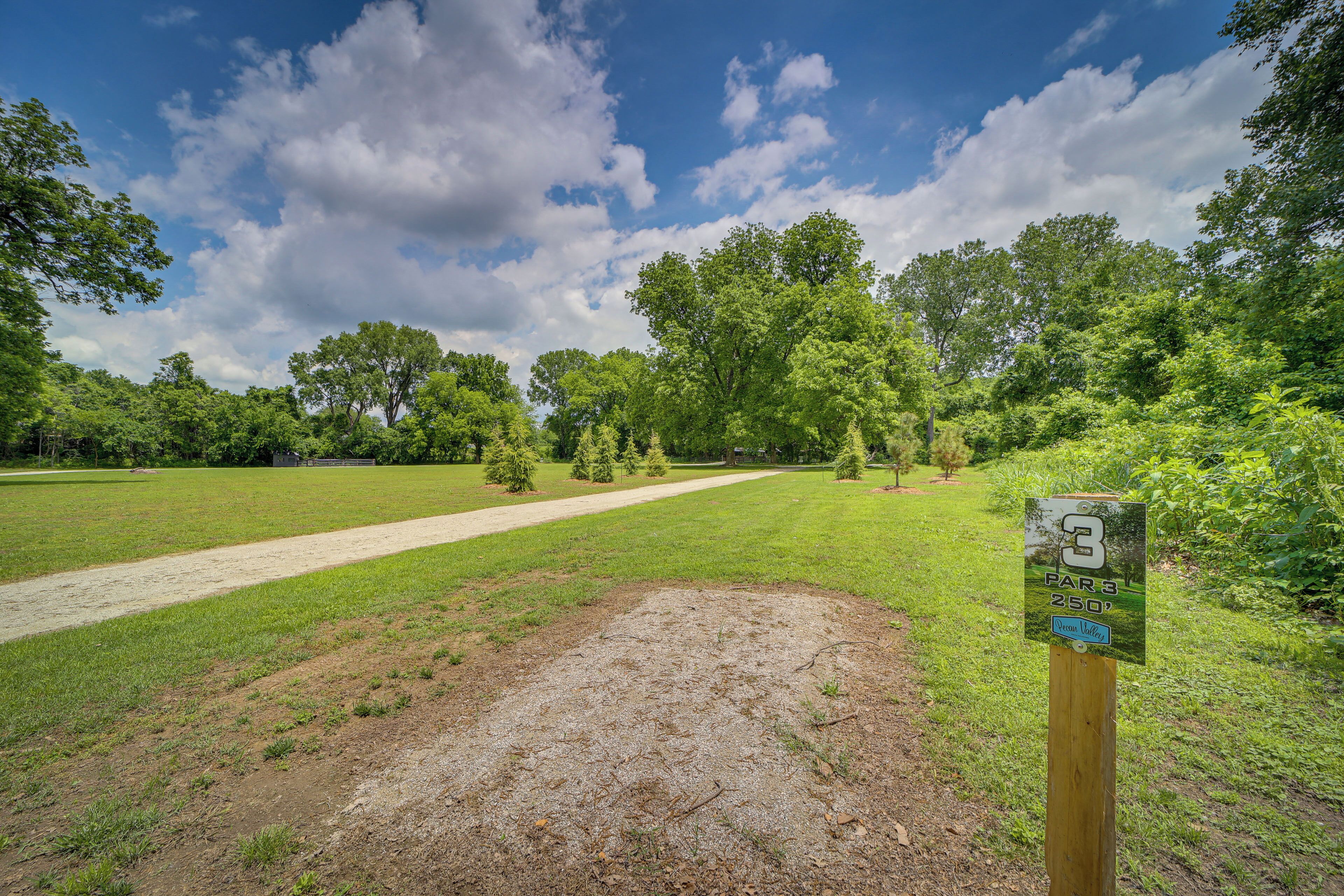 A golf course with a clear path, a sign indicating hole number 3, and a surrounding area of trees and grass.