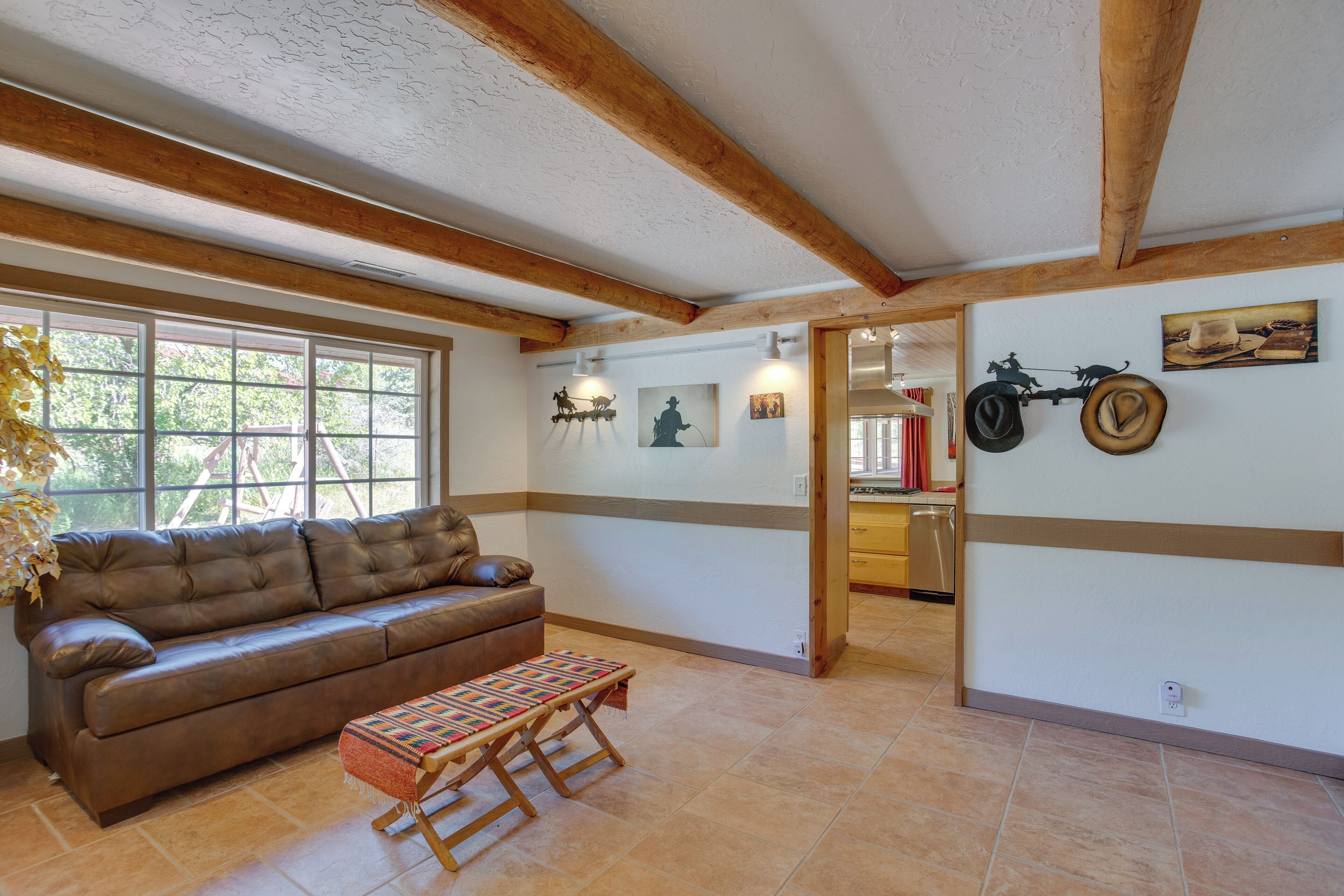 A spacious living room with a brown leather sofa, a wooden bench, and a large window.