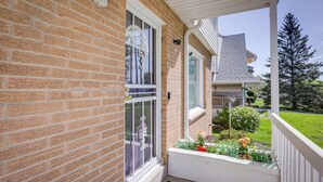 A brick house with a white porch, a window with a metal gate, and a small garden with flowers and plants. - Comfortable Milwaukee Abode ~ 10 Mi to Downtown! (Milwaukee)