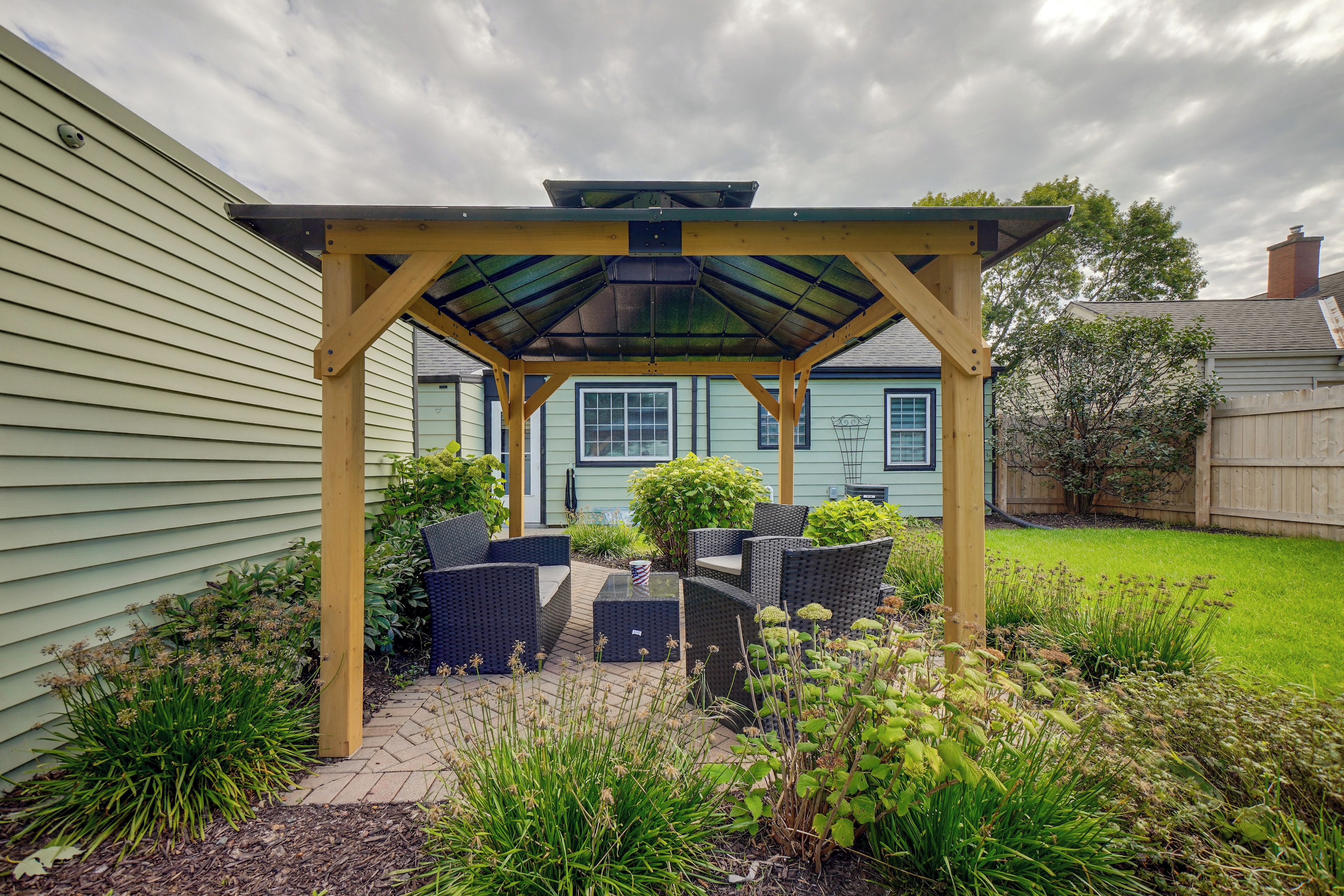 Ein überdachter Patio-Bereich mit Gartenmöbeln, einer Pergola und Blick auf ein Haus im Hintergrund.