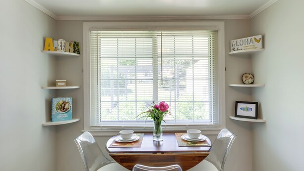 Un coin repas avec une table en bois, deux chaises, un vase de fleurs et des étagères remplies de livres et d’objets décoratifs.