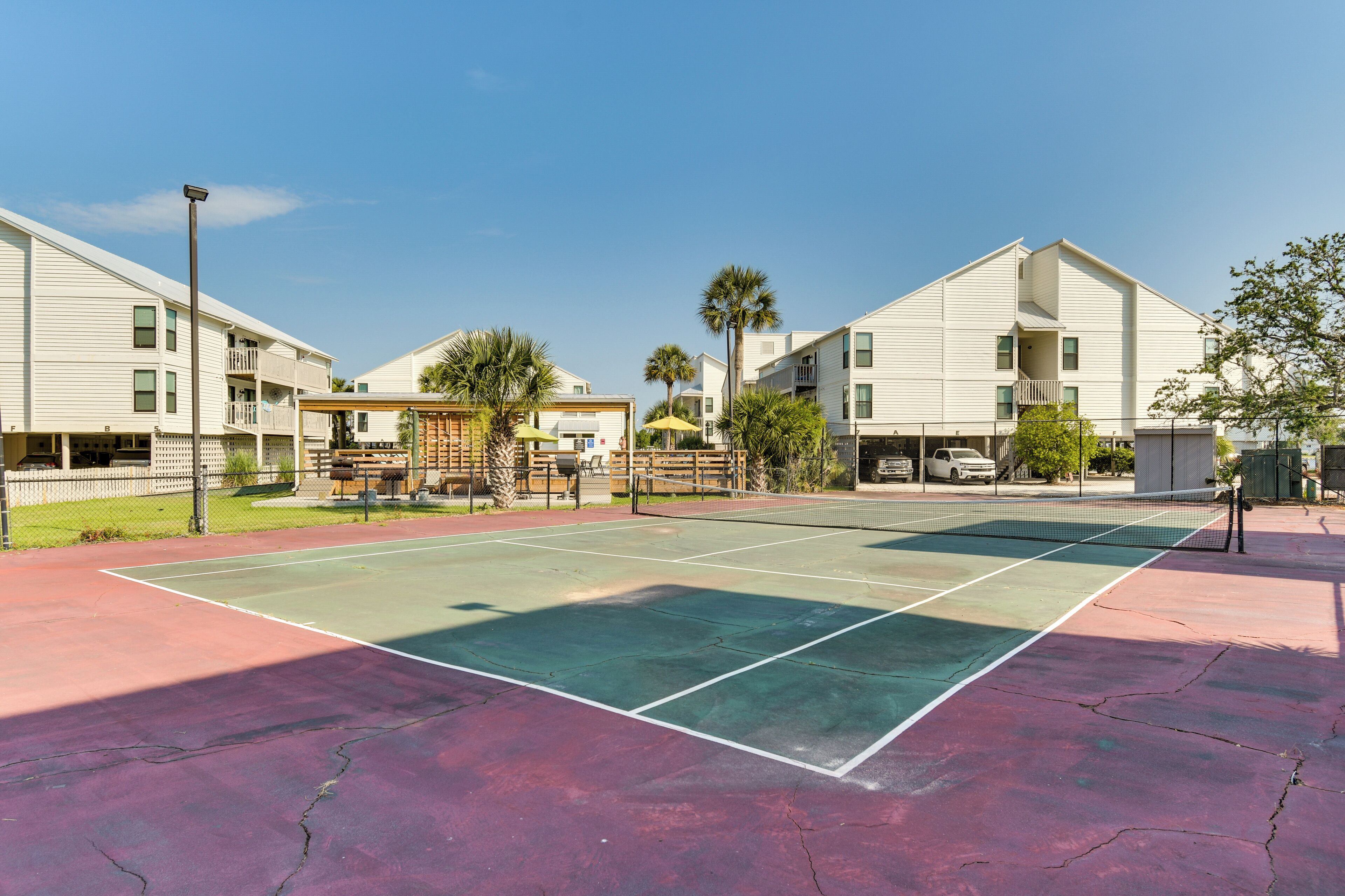 A tennis court with a net, surrounded by buildings with balconies and palm trees.