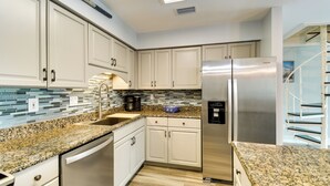 Eine moderne Küche mit weißen Schränken, einem Edelstahlkühlschrank, Granit Arbeitsplatten und einer gefliesten Rückwand.