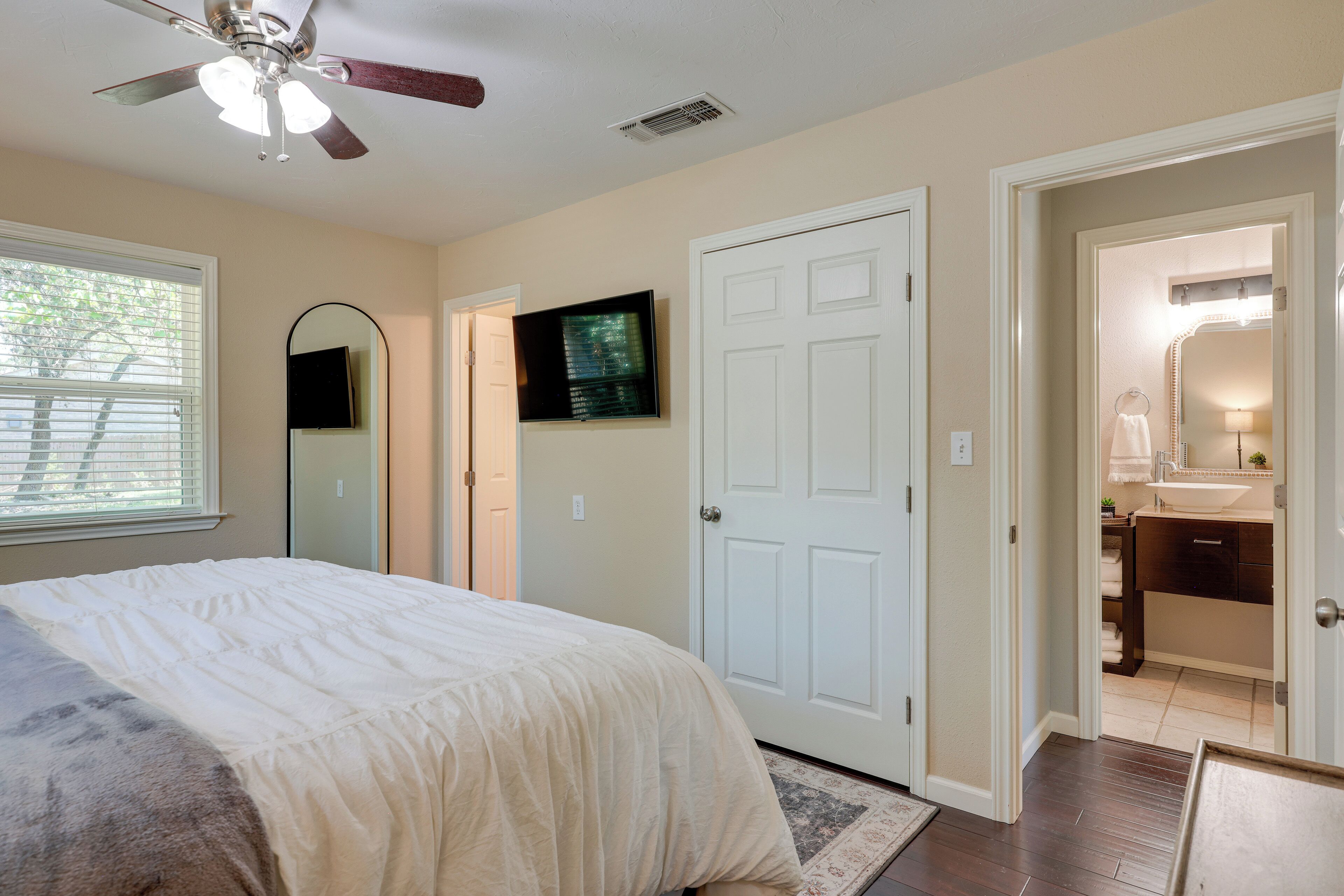 A bedroom with a bed, a ceiling fan, a TV, and a door leading to a bathroom.