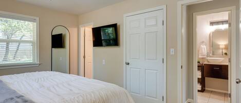 A bedroom with a bed, a ceiling fan, a TV, and a door leading to a bathroom.