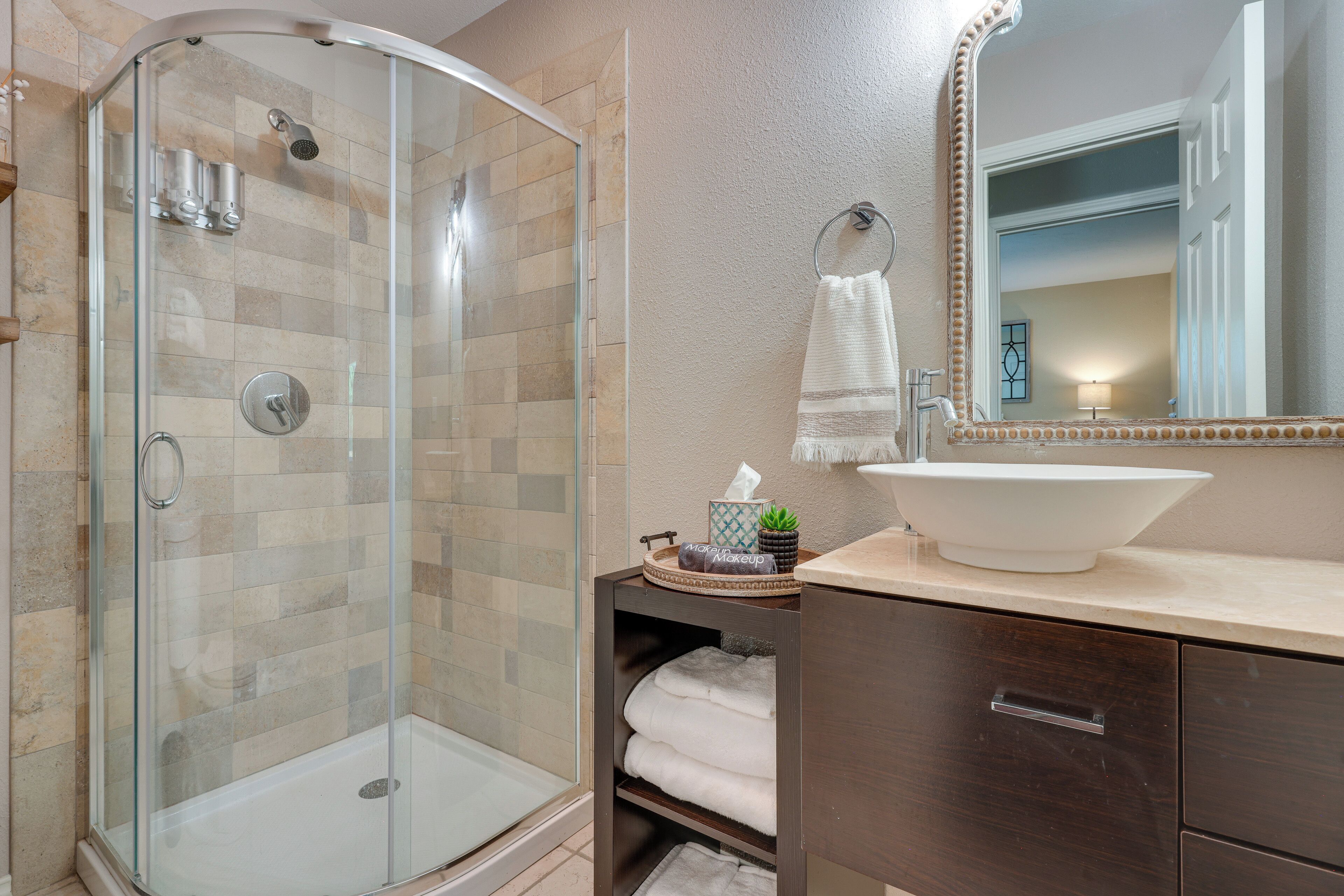 A modern bathroom with a glass-enclosed shower, a large mirror, and a sink with a towel rack.