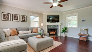 Ein Wohnzimmer mit Ecksofa, Kamin, Deckenventilator und gerahmten Kunstwerken an der Wand.