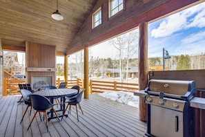 A covered outdoor deck with a grill, chairs, and a table.
