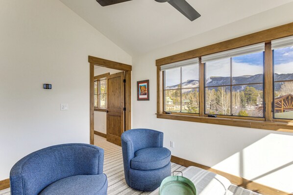 A room with two blue chairs, a window with a mountain view, and a wooden door.