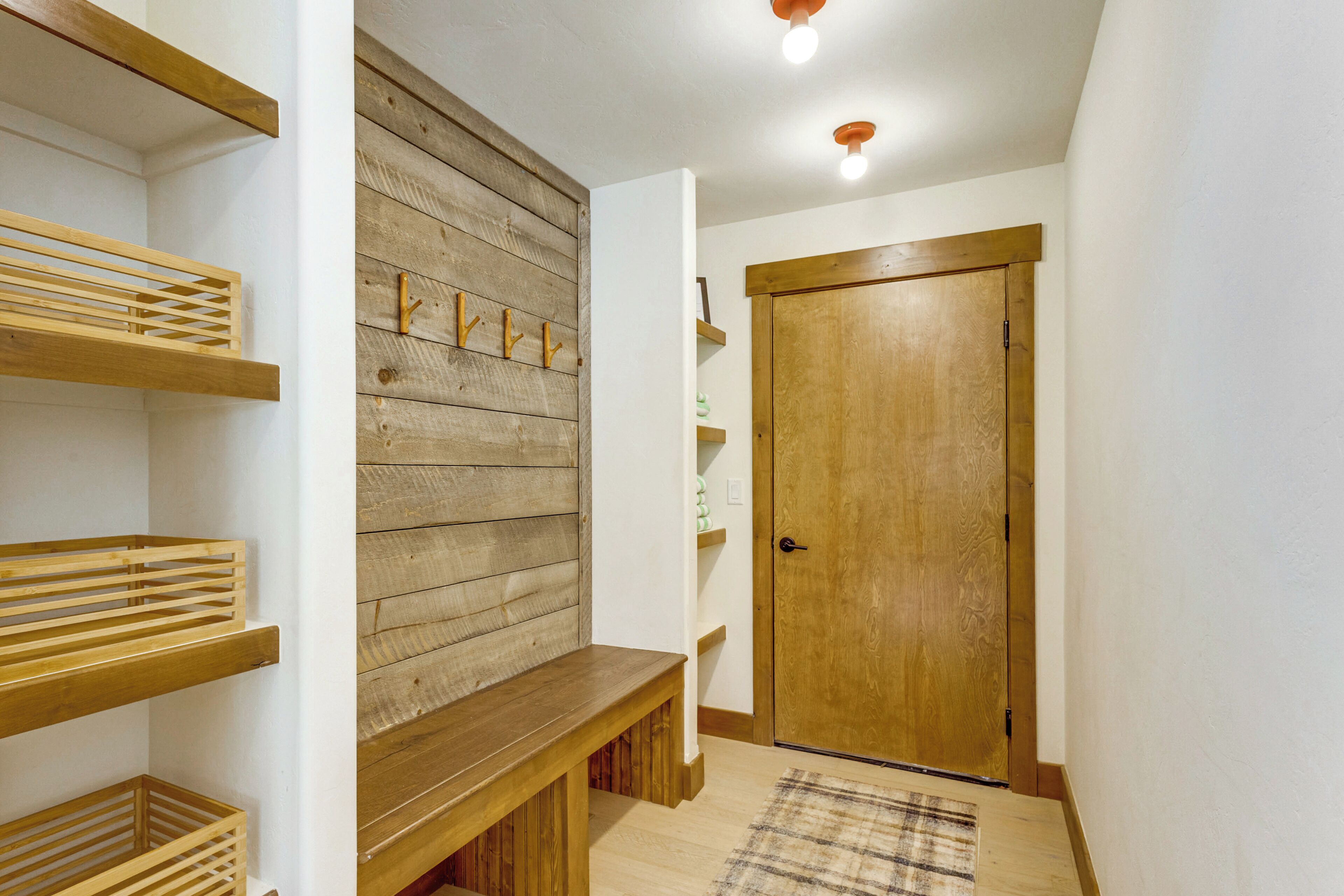 Ein Flur mit Holzböden, Regalen, einer Bank, einer Tür und einer Wand mit Holzvertäfelung.