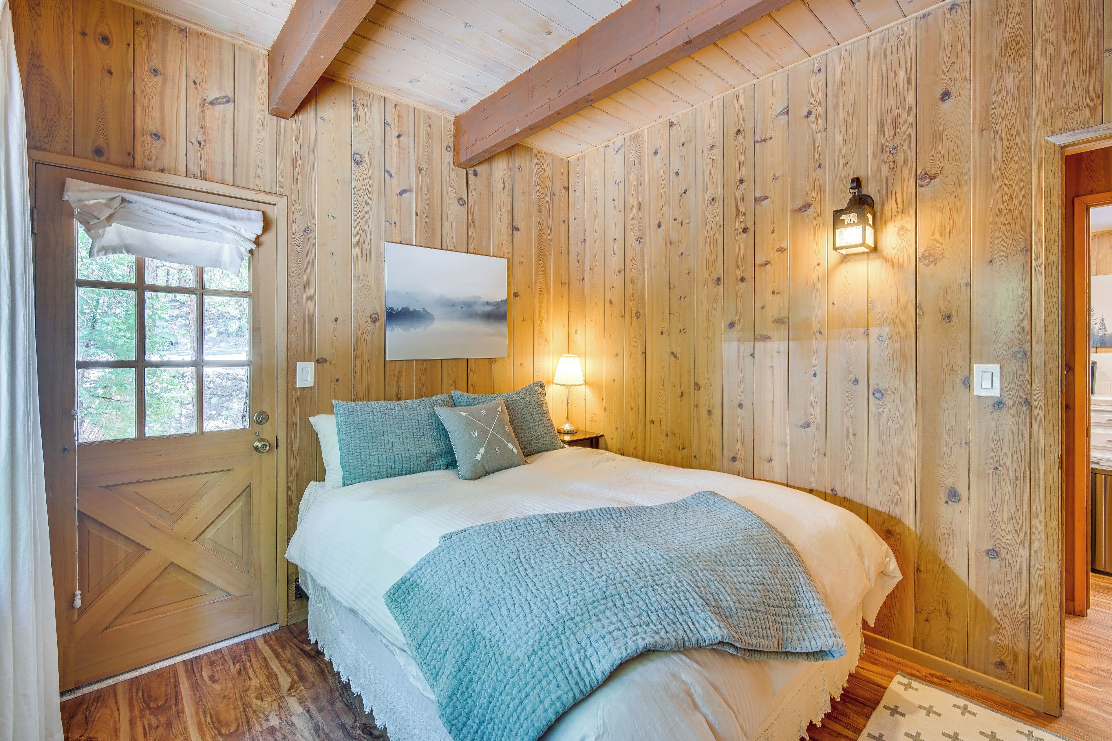 Quarto com painéis de madeira, uma cama, uma janela e luminária fixada na parede.