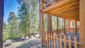 A wooden cabin with a porch and a wooden fence, surrounded by trees. - Crestline Area Vacation Rental Cabin w/ Decks! (Cedarpines Park)