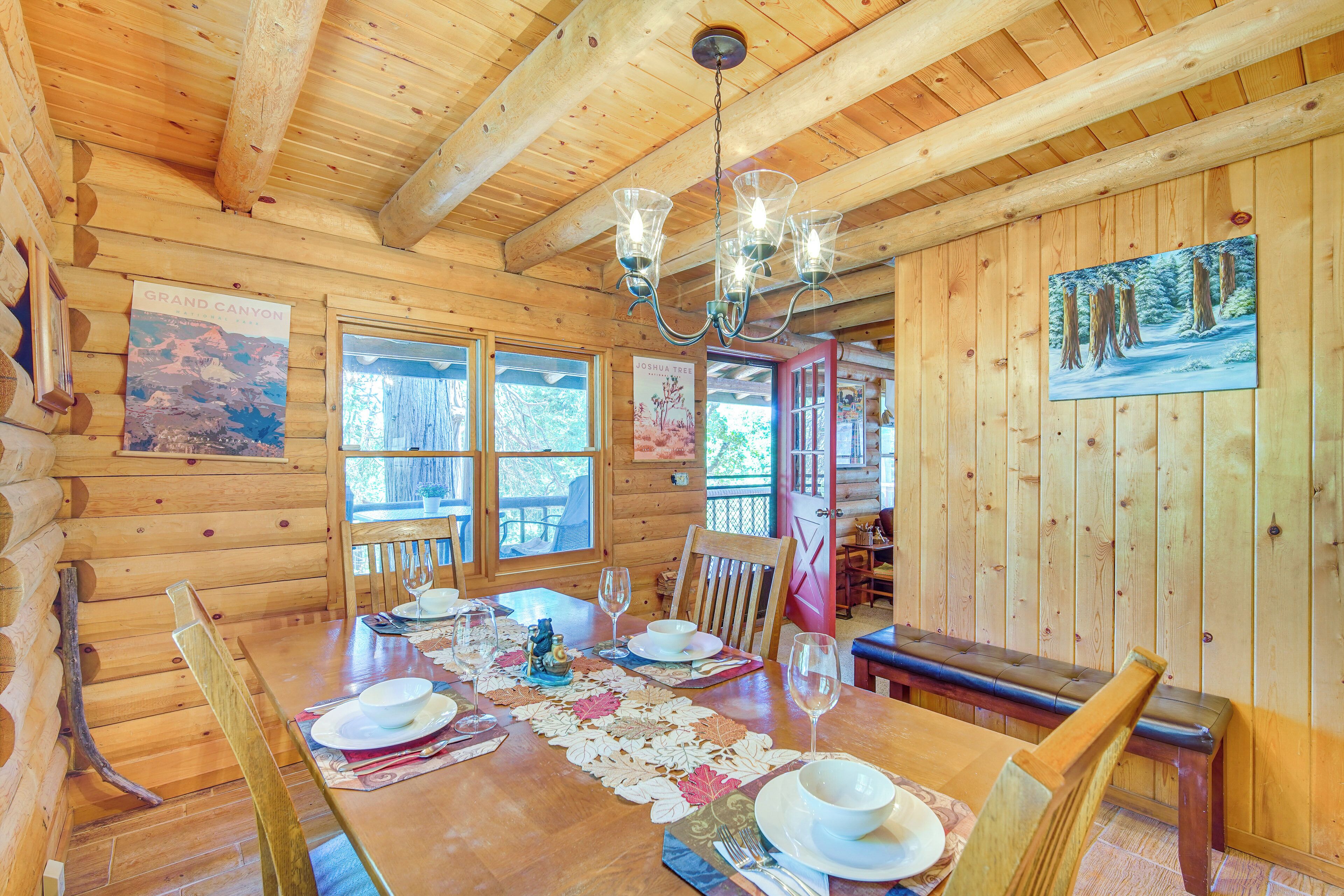 A wooden cabin dining area with a wooden table set for four, a chandelier, and a painting on the wall.