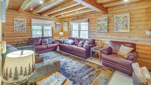A log cabin interior with wooden walls, a leather sofa, a coffee table, and a lamp. - Crestline Area Vacation Rental Cabin w/ Decks! (Cedarpines Park)