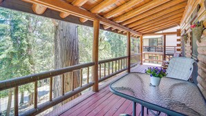 A wooden deck with a glass table and chairs, surrounded by a wooden railing and a view of trees. - Crestline Area Vacation Rental Cabin w/ Decks! (Cedarpines Park)
