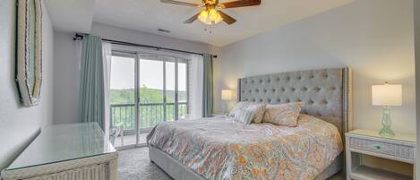 A bedroom with a large bed, a ceiling fan, a glass table, and a view of the outdoors.