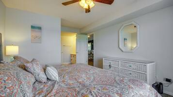 Un dormitorio con cama, ventilador de techo, cómoda, espejo y puerta que da a otra habitación.