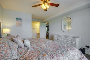 Een slaapkamer met een bed, een plafondventilator, een dressoir, een spiegel en een deur naar een andere kamer.