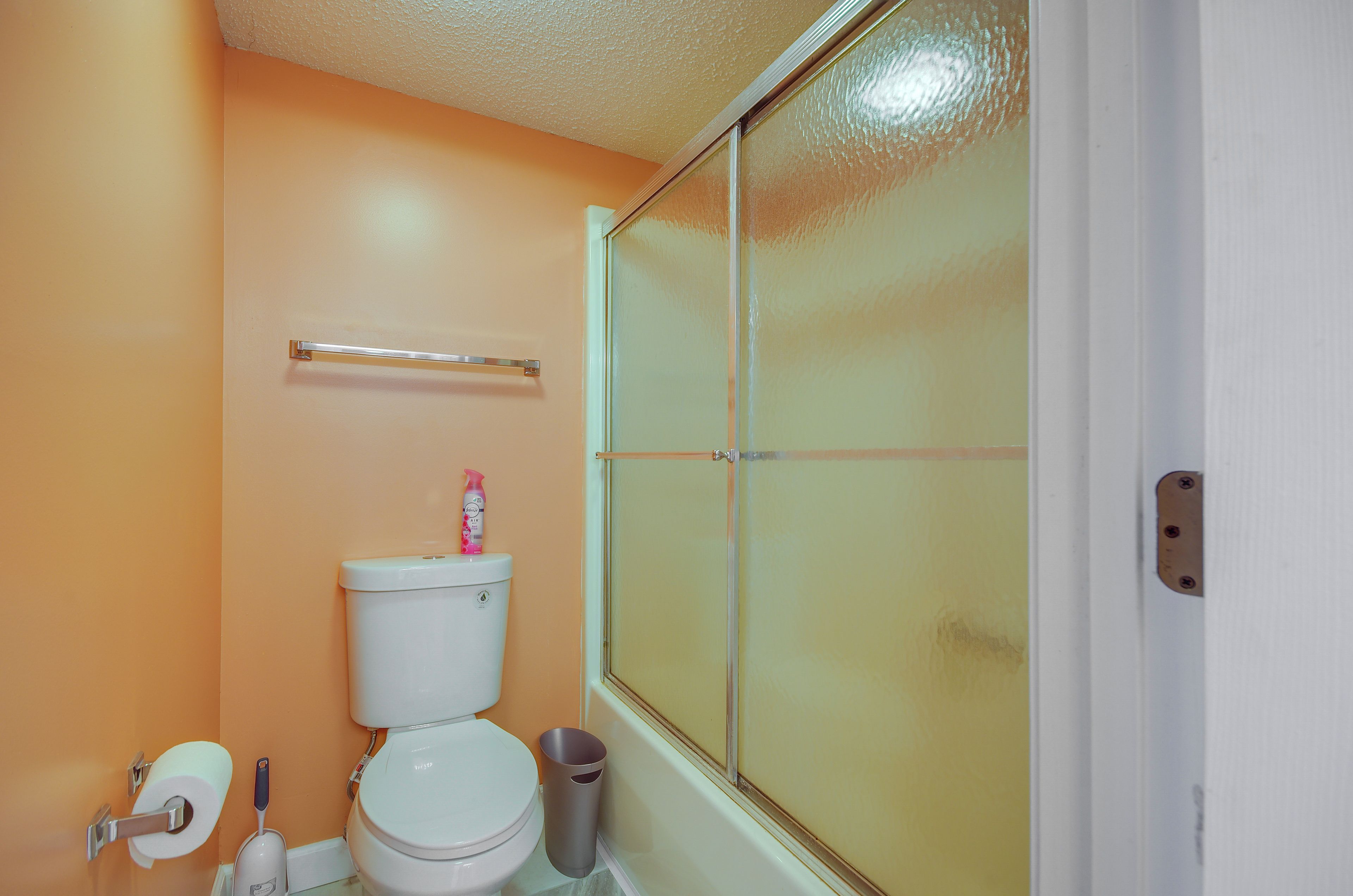 A bathroom with a toilet, a trash can, a toilet paper holder, and a shower door.