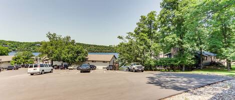 A parking lot with several vehicles, a building with a sloped roof, and surrounding trees.