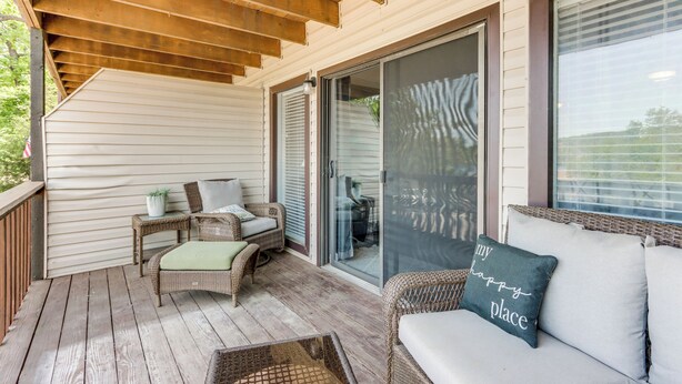 A covered porch with wicker furniture, a sliding glass door, and a cushion with text. - Pool Access & Lake View: Osage Beach Condo! (Osage Beach)