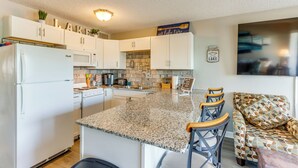 A kitchen with white cabinets, a granite countertop, and a seating area with patterned chairs. - Pool Access & Lake View: Osage Beach Condo! (Osage Beach)