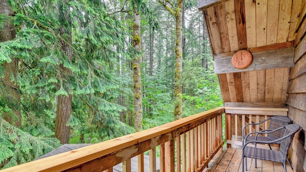 A wooden deck with a wooden railing, a wicker chair, and a wooden ceiling with a clock. - Peaceful Mt. Hood Cabin w/ Hot Tub & Fire Pit! (Rhododendron)