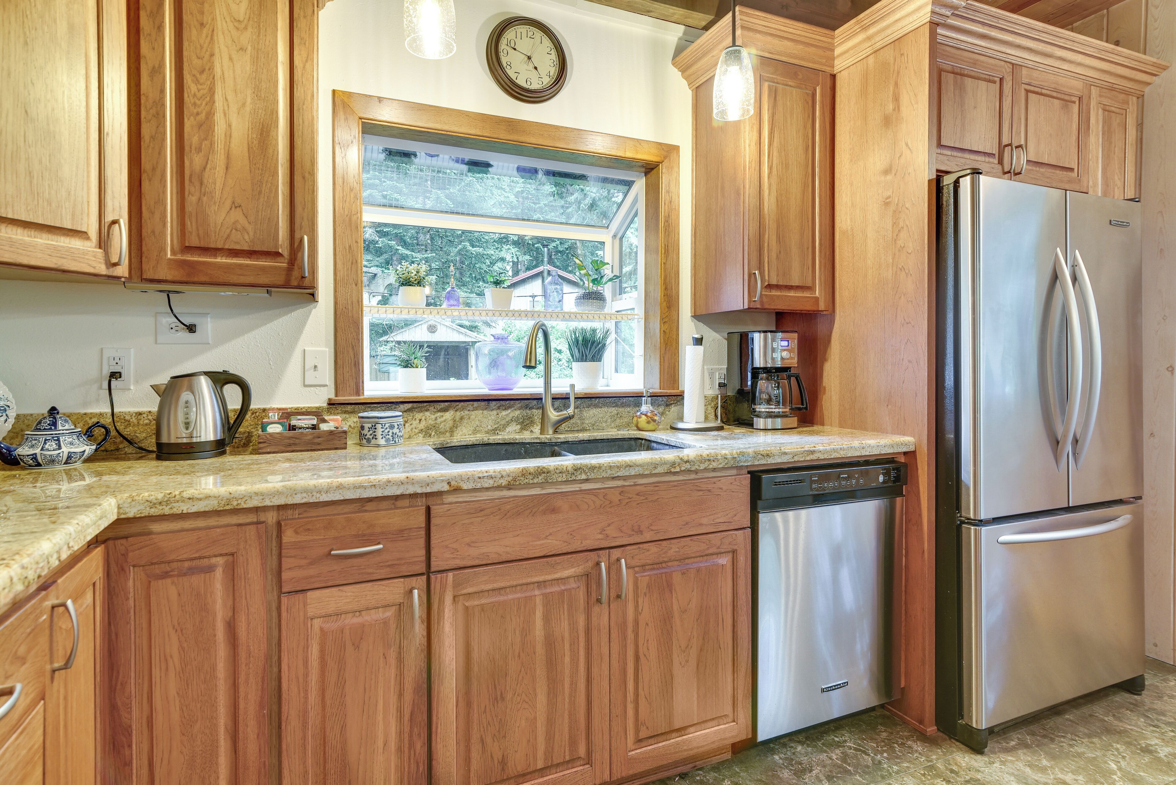 A kitchen with wooden cabinets, stainless steel appliances, a window with a view, and a clock on the wall.