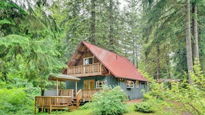 A cabin with a wooden deck and a red roof, surrounded by dense forest. - Peaceful Mt. Hood Cabin w/ Hot Tub & Fire Pit! (Rhododendron)