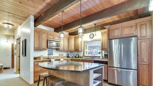 A kitchen with wooden cabinets, a stainless steel refrigerator, and a bar area with stools. - Peaceful Mt. Hood Cabin w/ Hot Tub & Fire Pit! (Rhododendron)