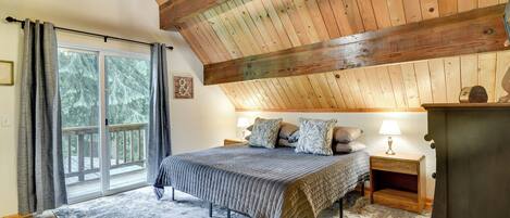 Quarto com cama grande, mesa de cabeceira, cômoda, lustre e porta de vidro deslizante que dá para uma varanda.