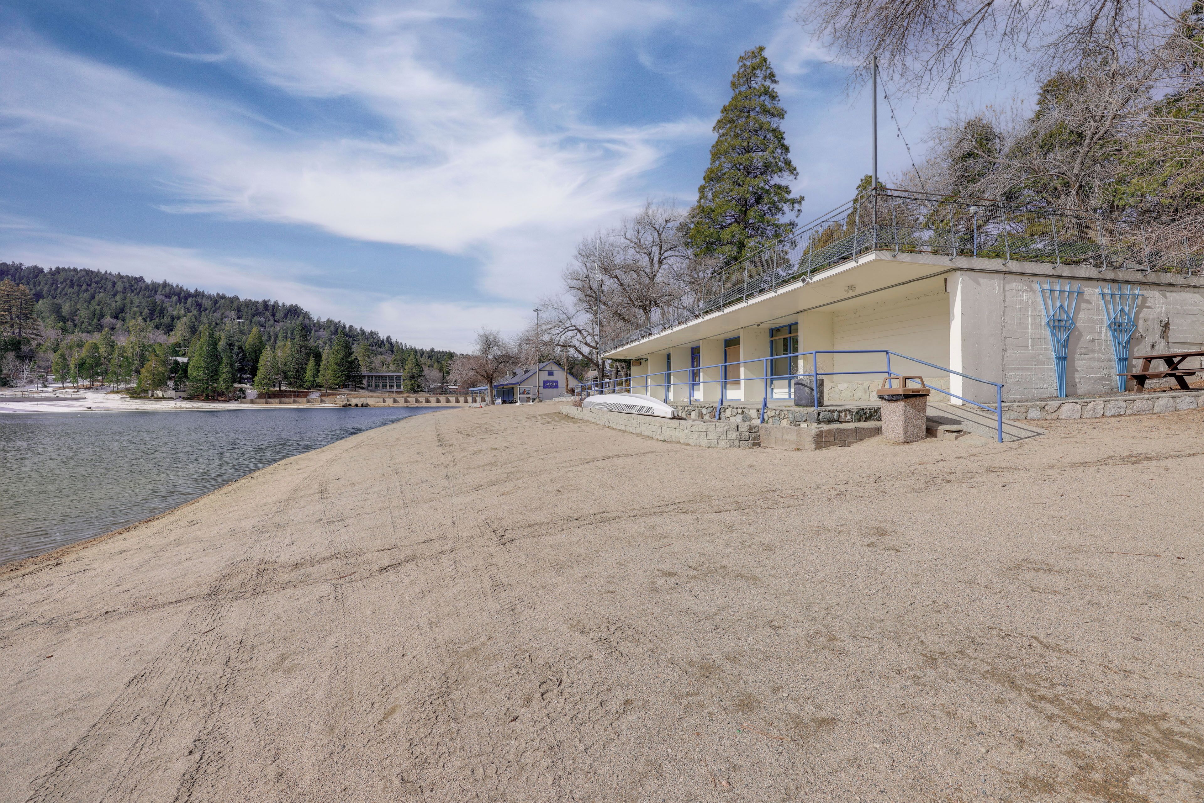 A beachside building with a sandy foreground, a clear sky, and a forested hill in the background.