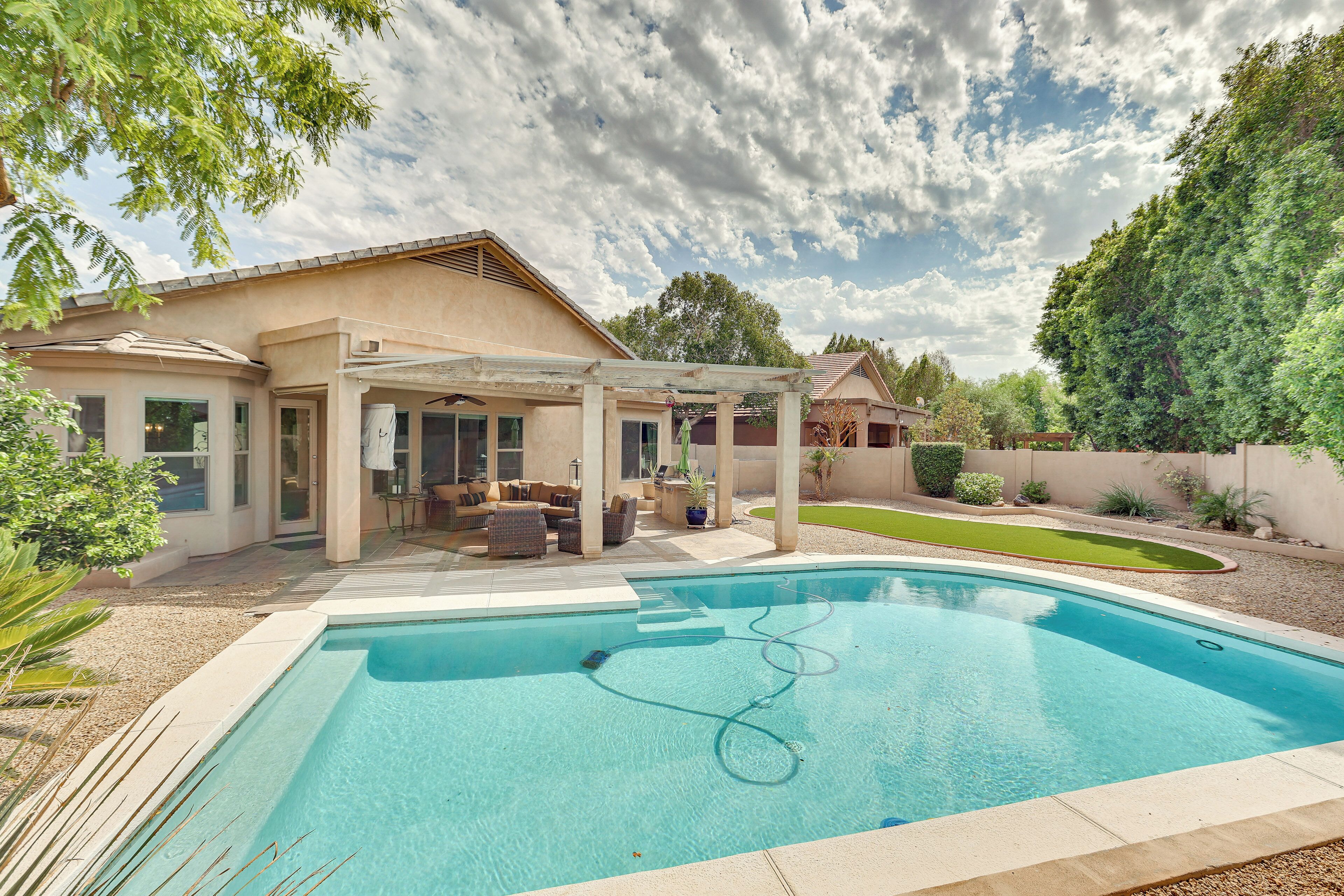 A backyard with a swimming pool, a covered patio area, and a well-maintained lawn.