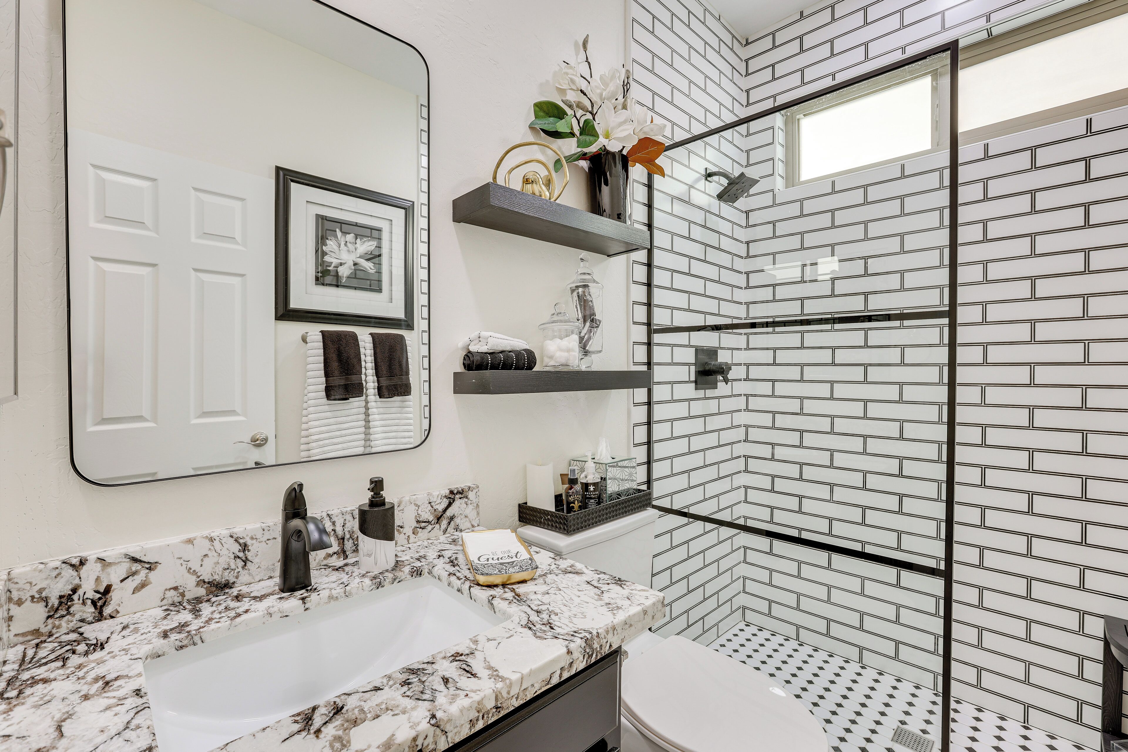 Un baño con lavamanos blanco, un espejo grande, ducha con puerta de vidrio y un inodoro blanco.