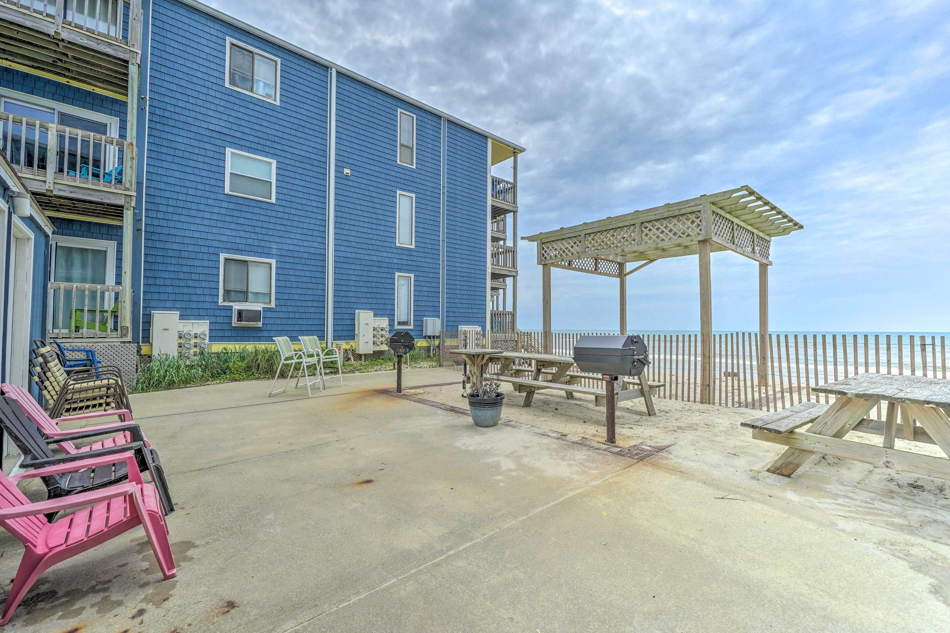 A beachfront building with a patio area featuring picnic tables, a grill, and outdoor seating.