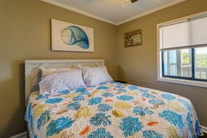 Quarto com cama, janela com persianas, parede com pintura e um letreiro decorativo.