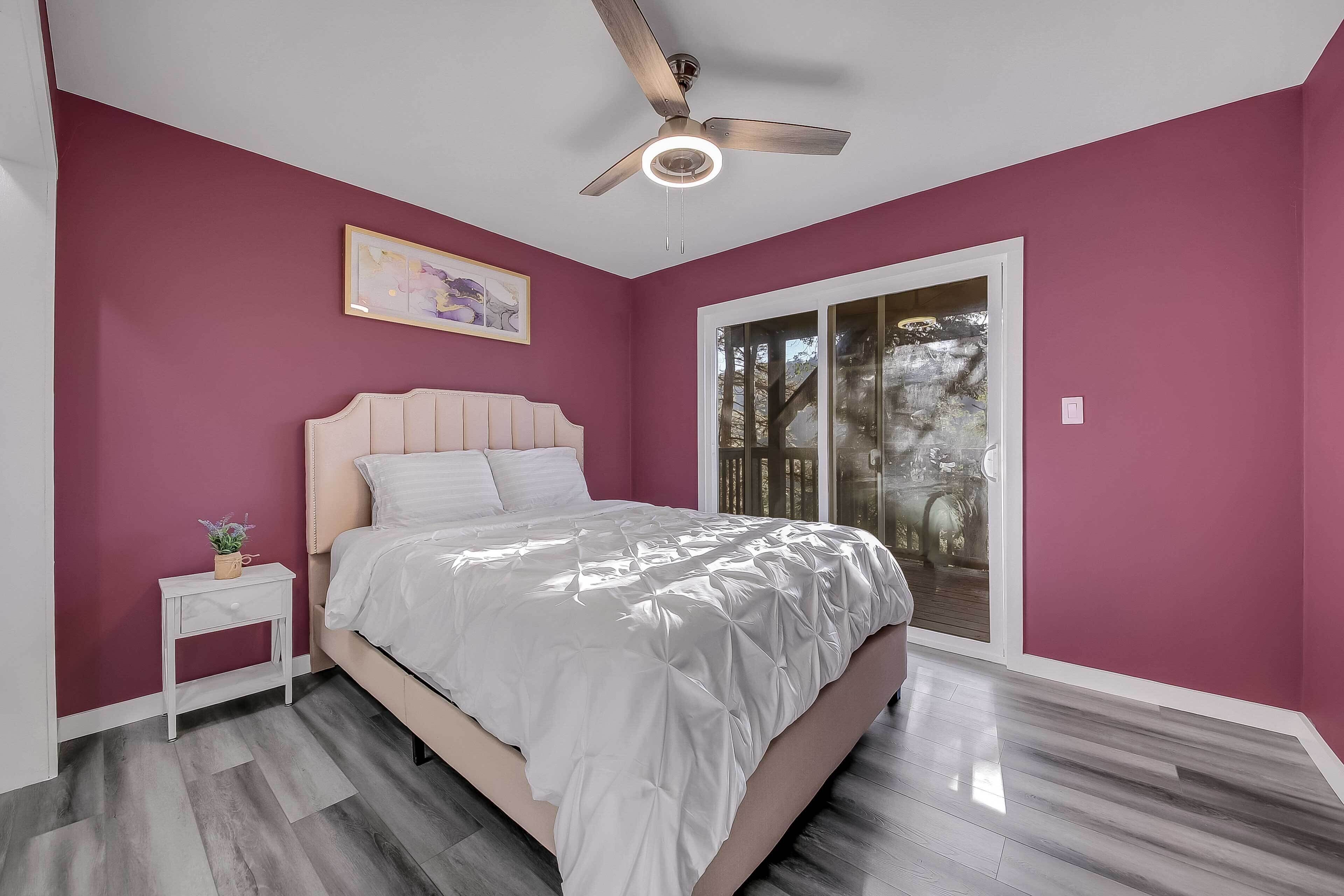 A bedroom with a bed, a nightstand, a ceiling fan, and a window with a view of trees.