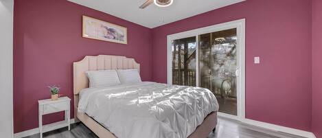 A bedroom with a bed, a nightstand, a ceiling fan, and a window with a view of trees.