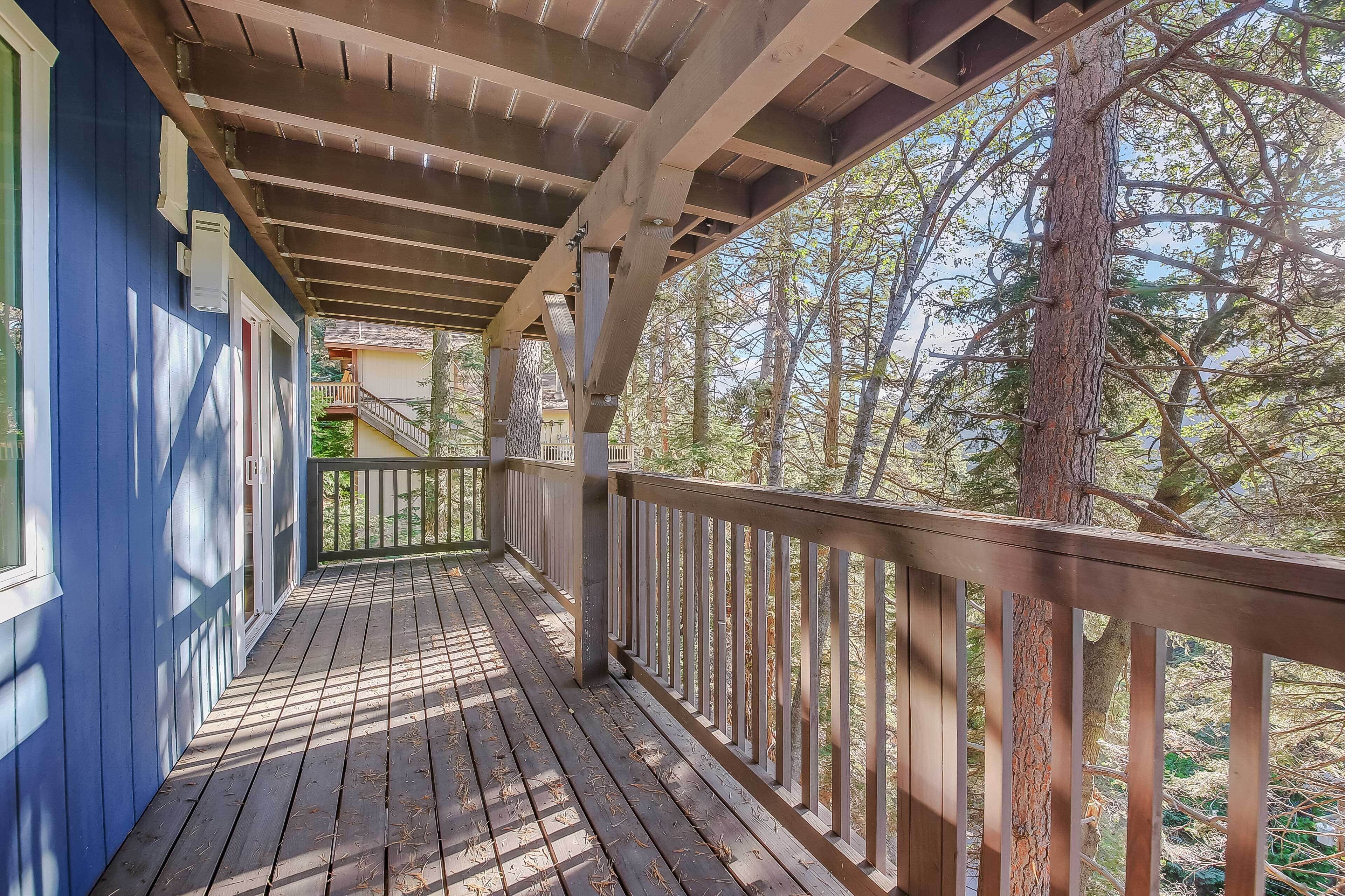 A wooden deck with a railing, overlooking a forested area.