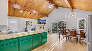 Een moderne keuken met groene kastjes, houten balken in het plafond en een eethoek met een groot raam.