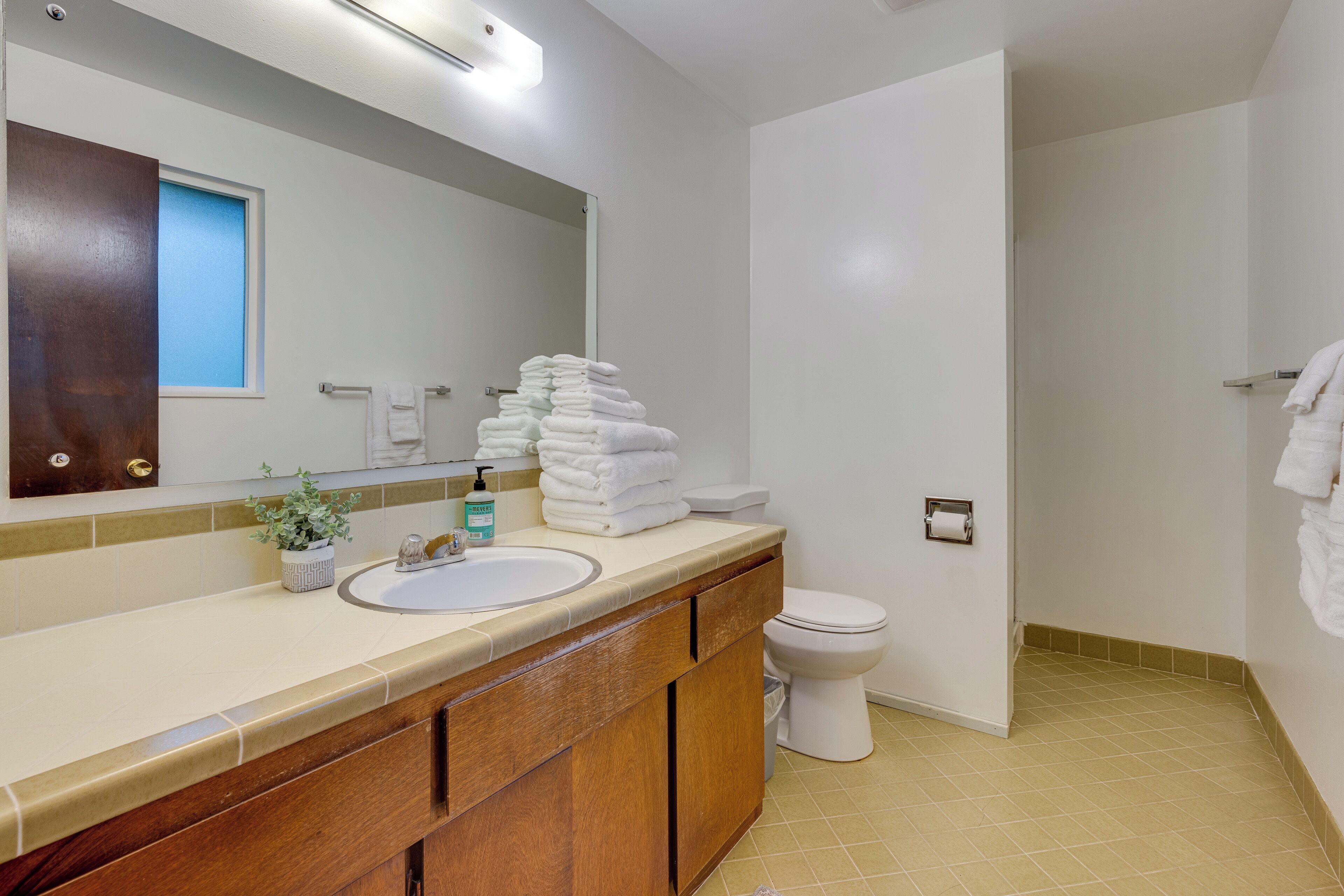 Et badeværelse med vask, spejl og toilet. Der ligger en stak hvide håndklæder på bordet.