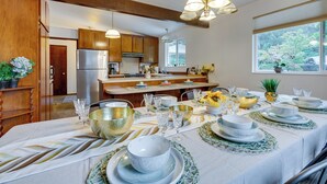 A modern kitchen with wooden cabinets, stainless steel appliances, and a dining area set for a meal with glassware and plates. - Expansive Lake Forest Park Home w/ Private Deck! (Lake Forest Park)