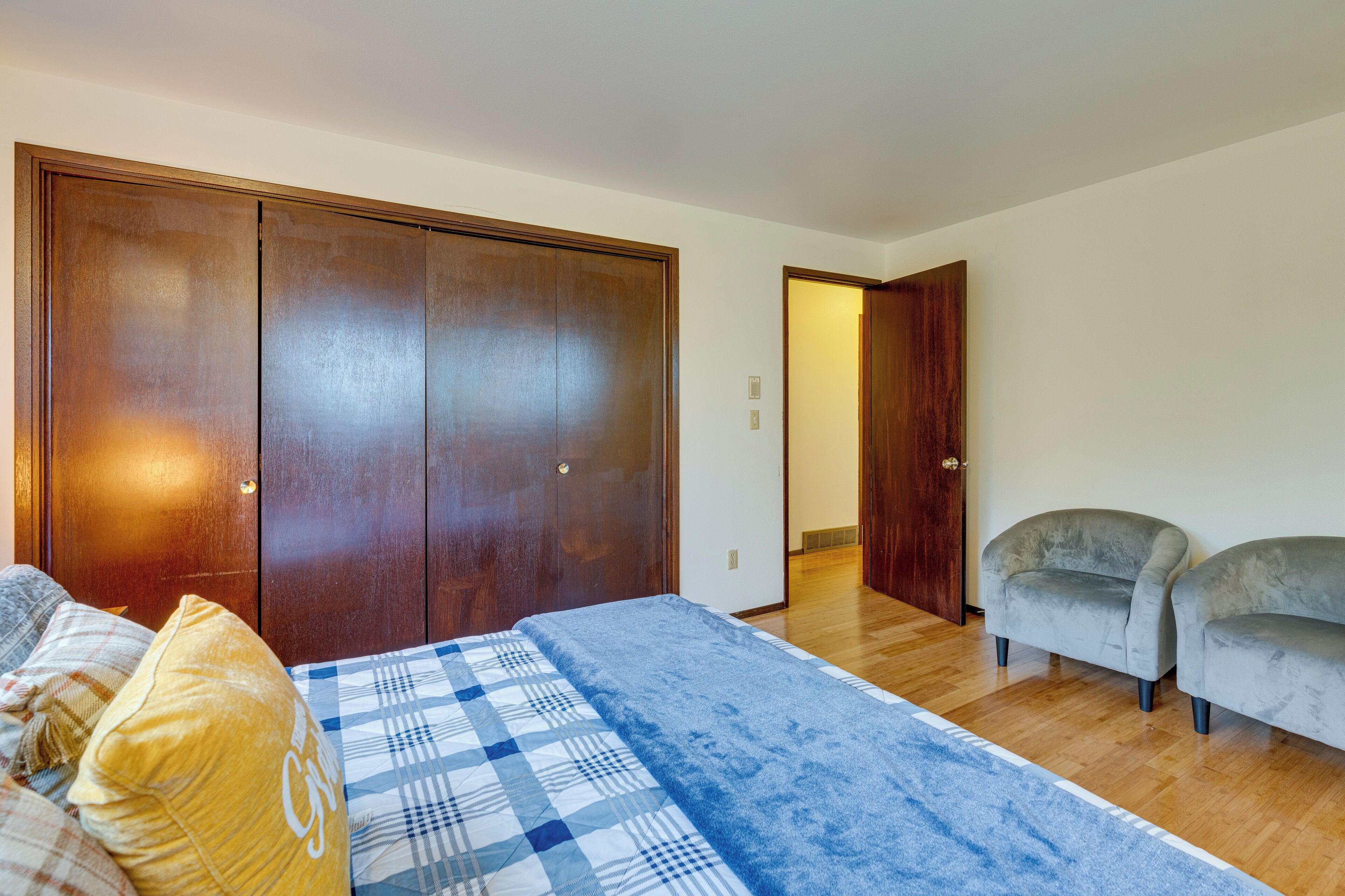 Ein Schlafzimmer mit großem Kleiderschrank, einem Bett mit blau-weiß karierter Bettdecke, zwei Sesseln und Holzboden.