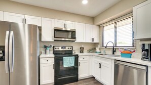 A modern kitchen with stainless steel appliances, white cabinetry, and a wooden floor.