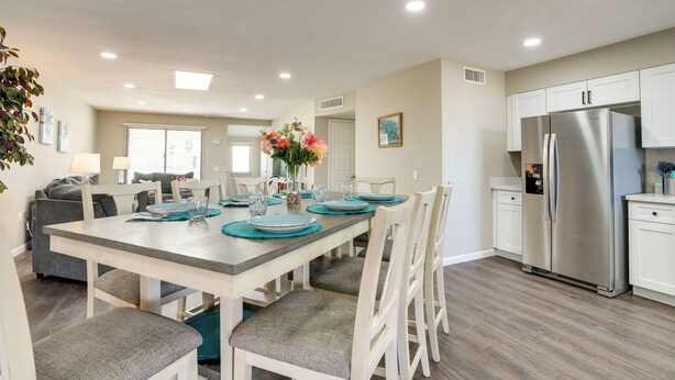 A modern kitchen with white cabinets, a stainless steel refrigerator, and a dining area with a wooden table and chairs.