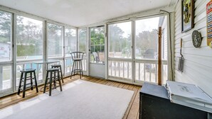 Una sala de estar con ventanales amplios, alfombra blanca, dos taburetes y una mesa de metal.