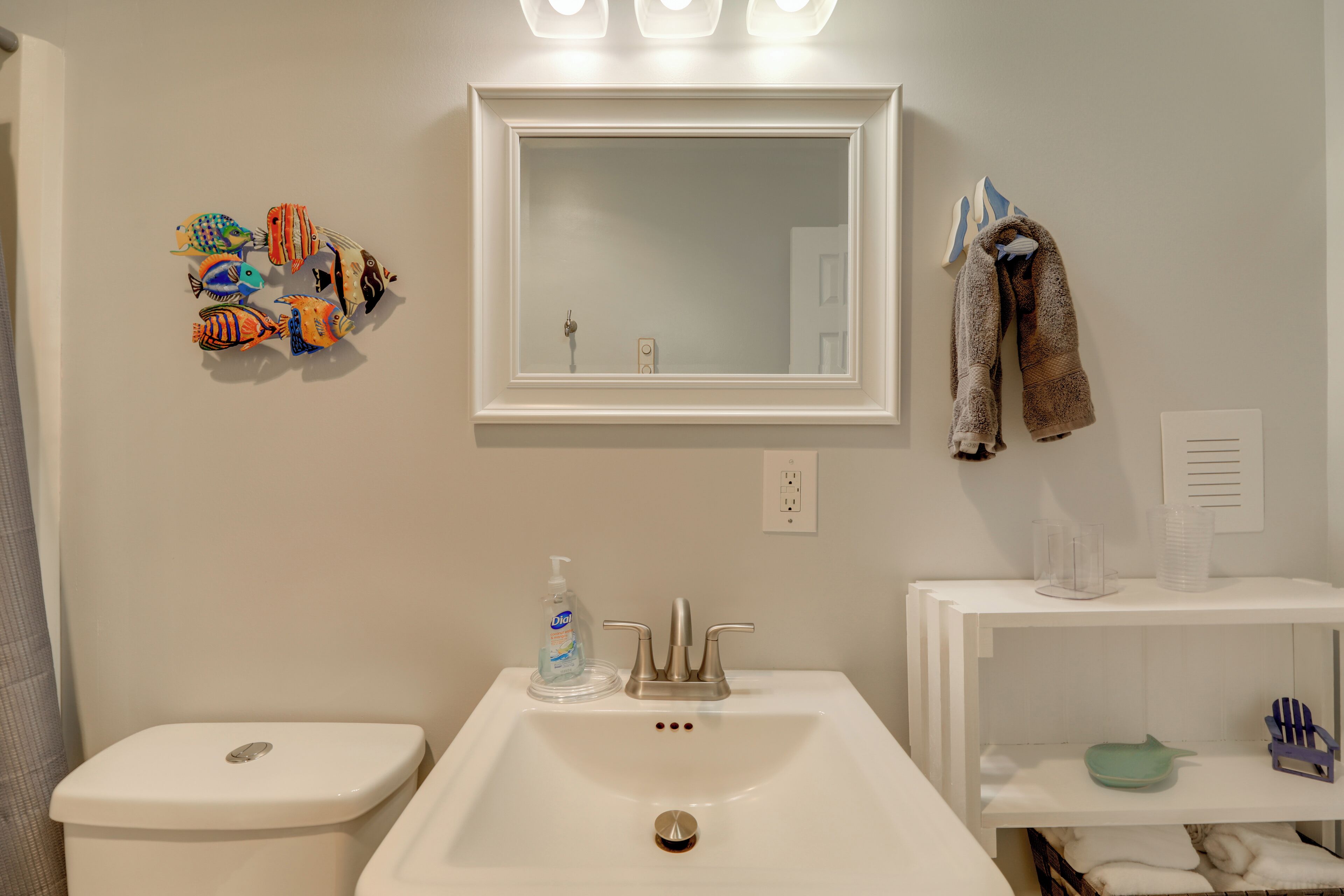 Een badkamer met een witte wastafel, toilet, spiegel en een plank met toiletartikelen.