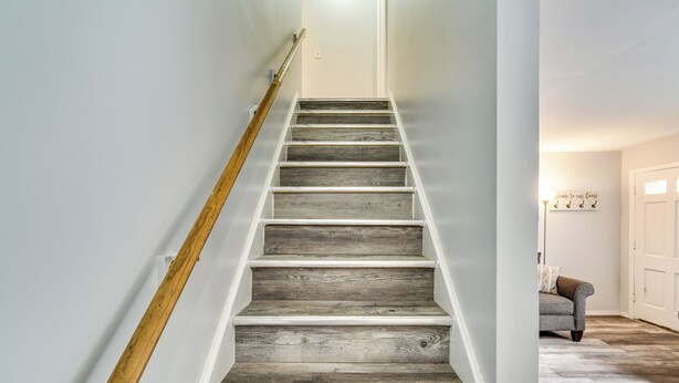 A staircase with wooden steps and a wooden handrail, leading to a room with a white door and a sign on the wall. - 4 Mi to Dtwn Rochester: Charming Apt w/ Patio! (Rochester)
