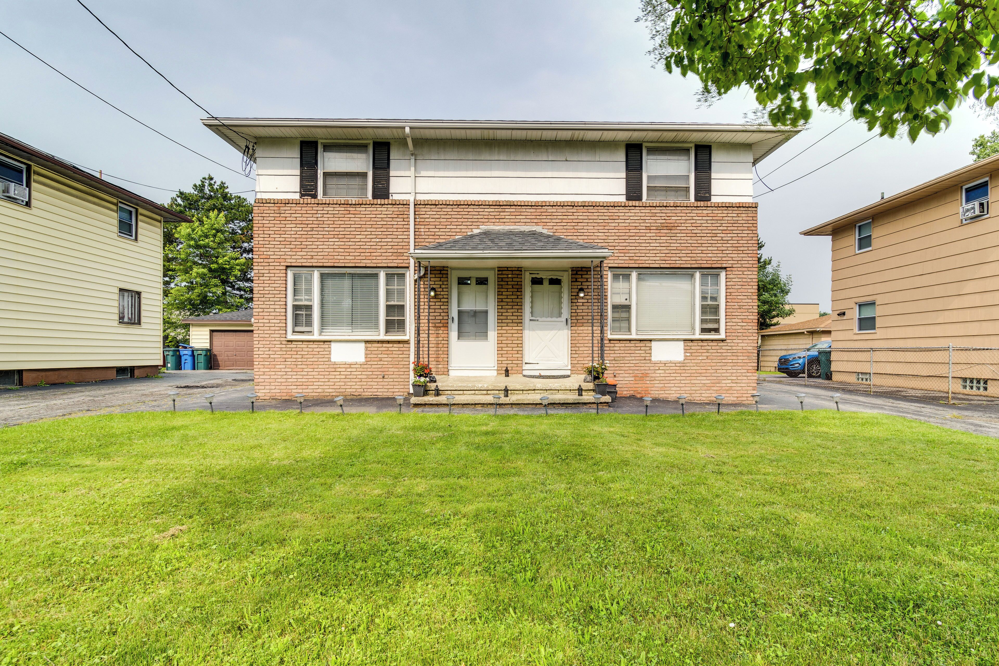 A two-story brick house with a front porch, a small front yard, and a garage.