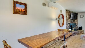 A dining area with a wooden table and chairs, a fireplace, a TV mounted on the wall, and a clock. - Joshua Tree Home w/ Patio - 5 Mi to National Park! (Joshua Tree)